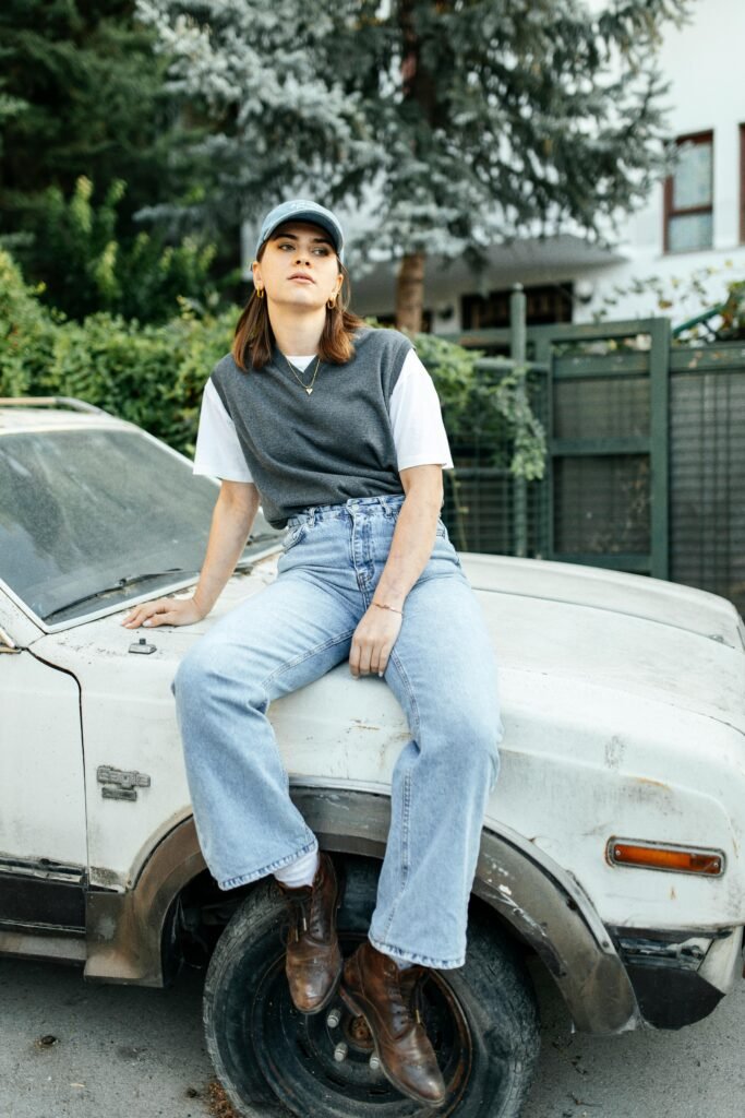 Stylish woman in casual attire sitting on a vintage car outdoors. Perfect for urban lifestyle themes.