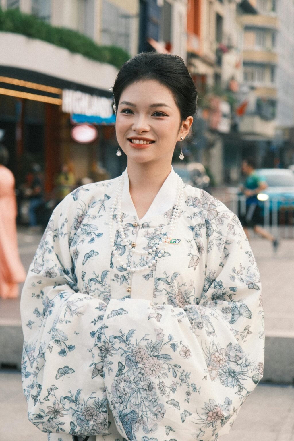 Smiling woman in a floral hanbok outdoors in an urban setting.