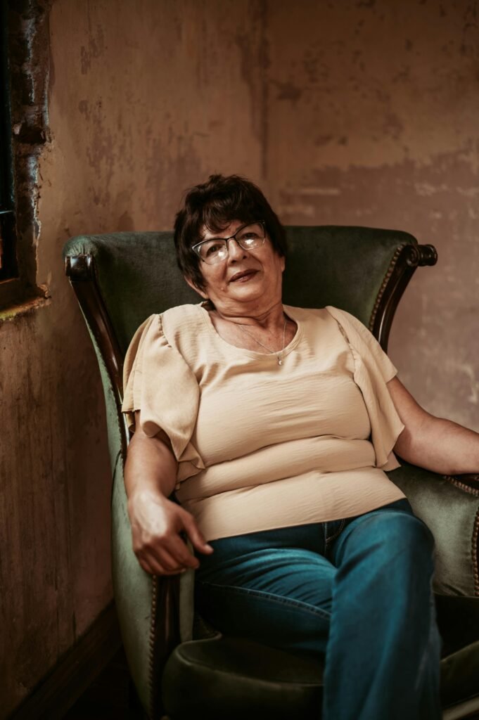 Elderly woman sitting comfortably in an aged vintage room with natural light.