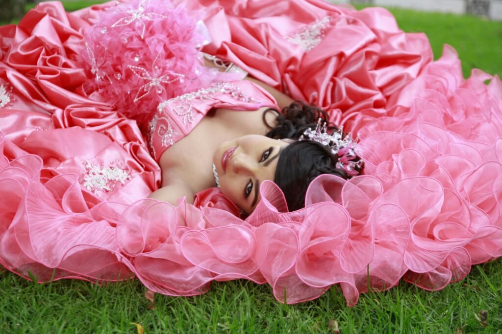 Beautiful quinceañera girl in a pink gown lying on grass, exuding elegance and charm.