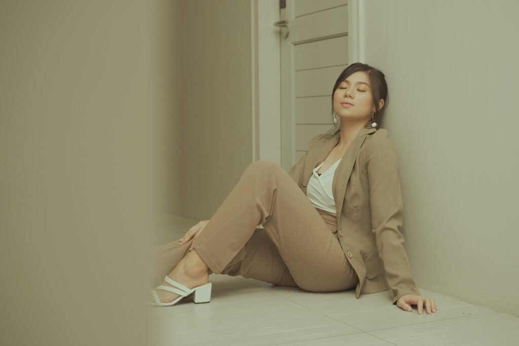 Businesswoman in a beige suit relaxing against a wall in a hallway, exemplifying modern fashion.